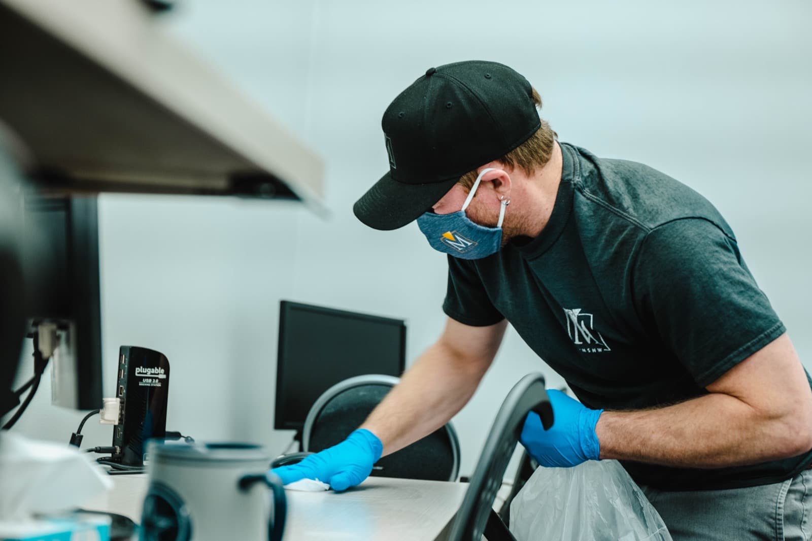 A masked, gloved crew member disinfecting a workstation